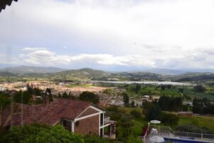Vista de un pueblo con un edificio destacado al frente, una masa de agua a lo lejos y colinas onduladas en el fondo.