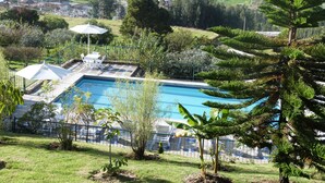 Zona de piscina con vista a una zona residencial, rodeada de vegetación y una valla.