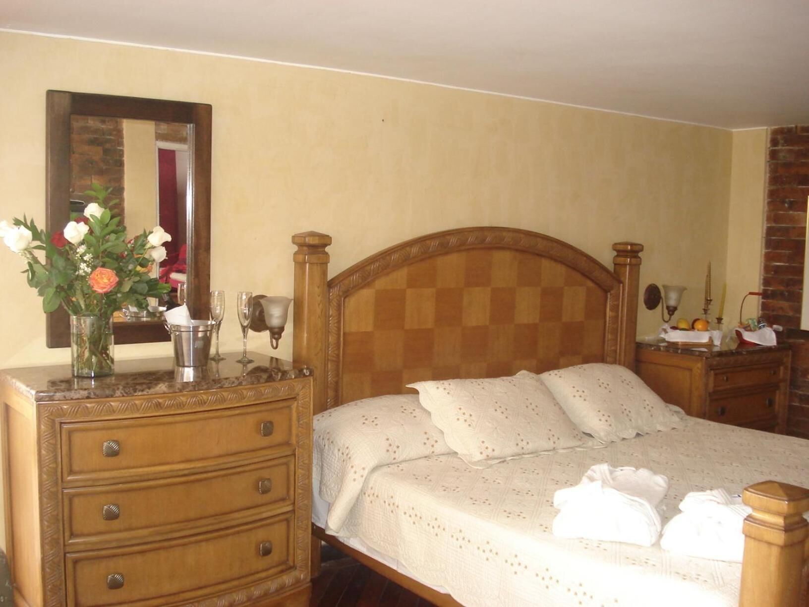 Un dormitorio con una cama de madera, un aparador con cajones, un espejo y un florero con flores.