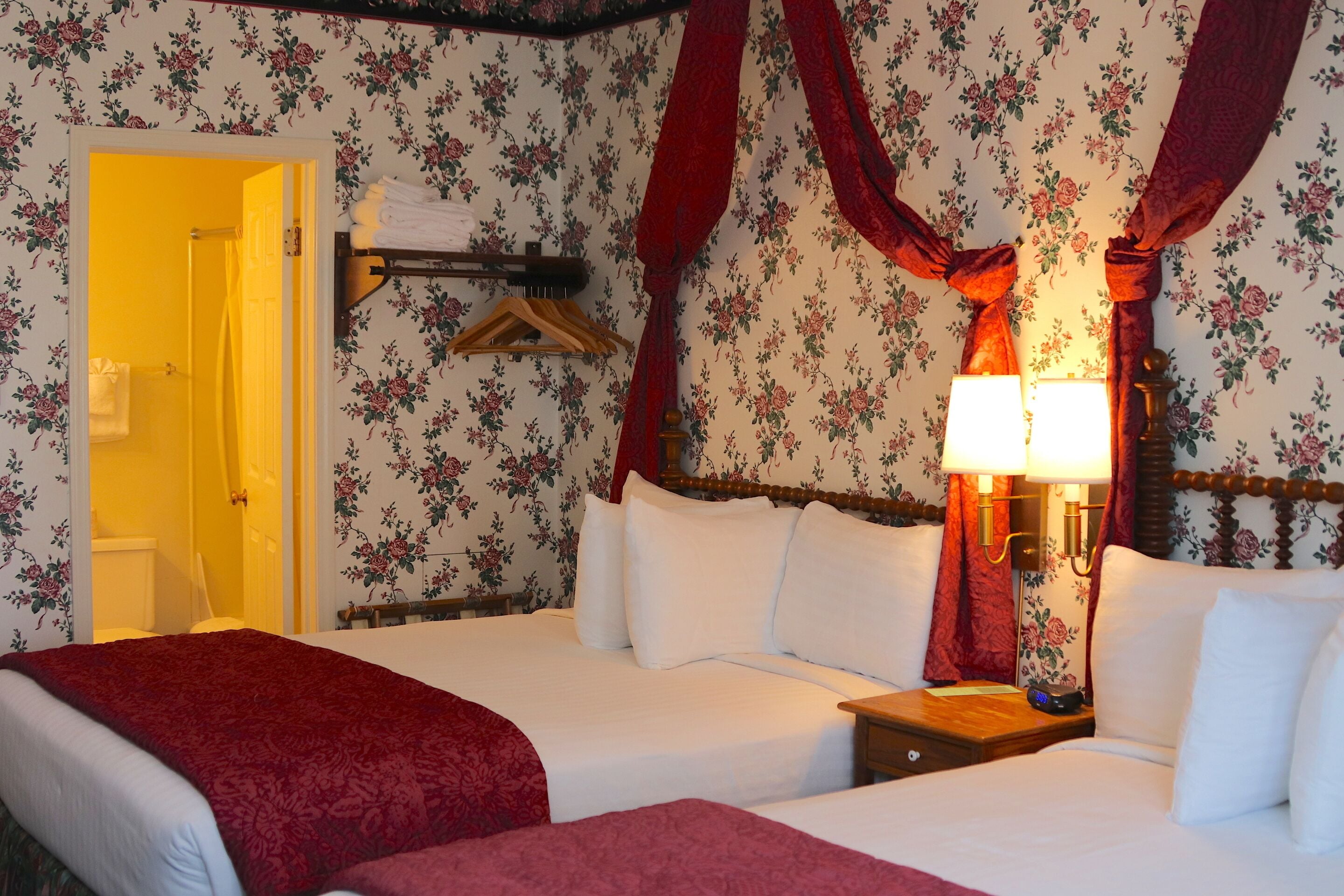 A hotel room with floral wallpaper, a bed with white linens, a bedside table with a lamp, and a wooden headboard.