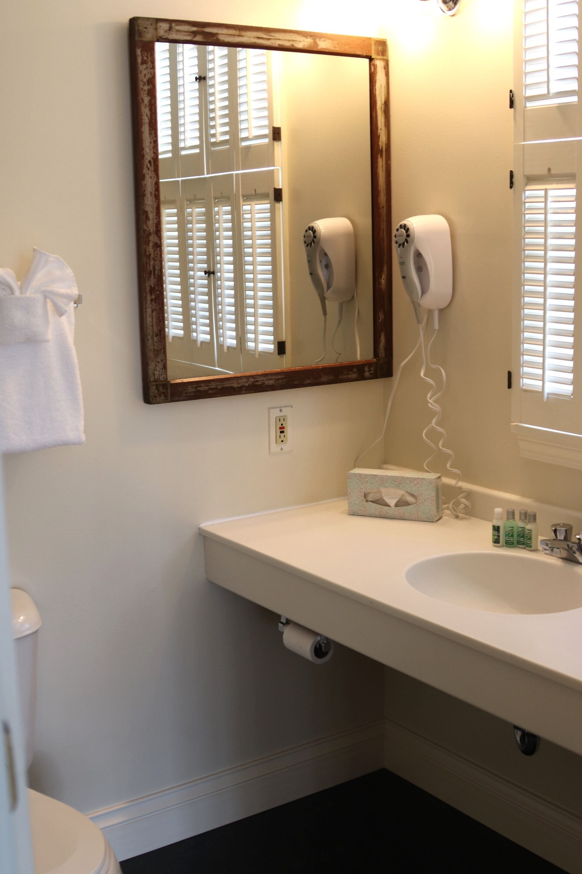 A bathroom with a white sink, a mirror with a wooden frame, a hairdryer, and a towel rack.