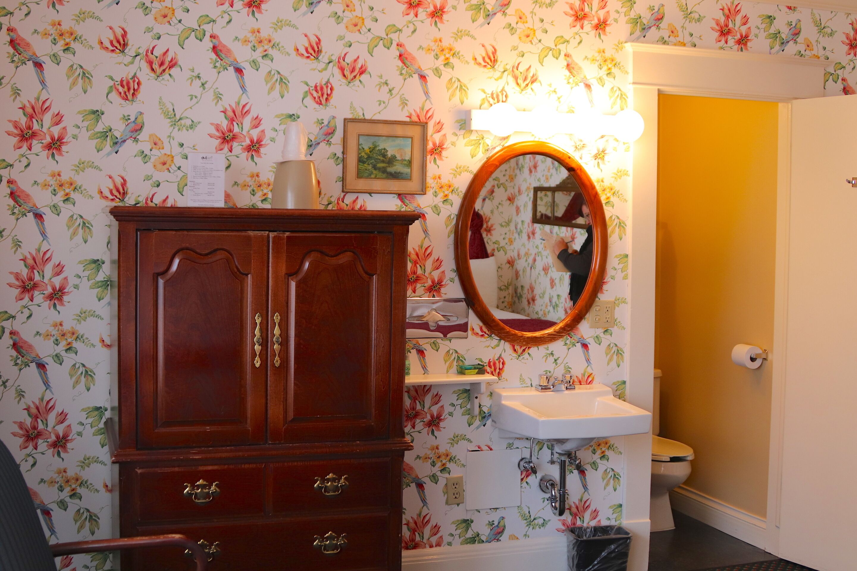 Un baño con papel tapiz floral, un mueble de madera, un espejo y un lavabo.