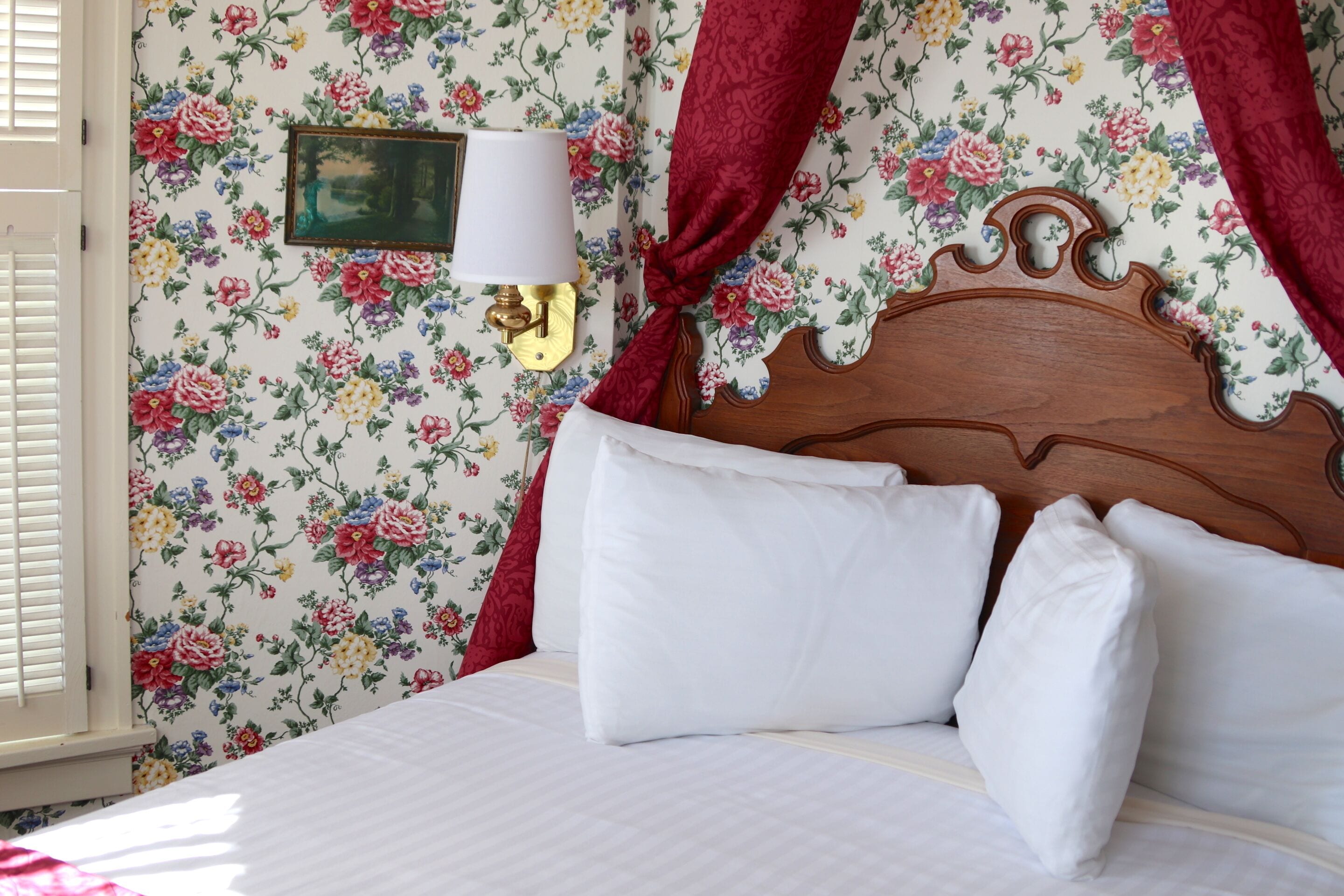 A bed with white bedding, a wooden headboard, and a floral wallpaper pattern.