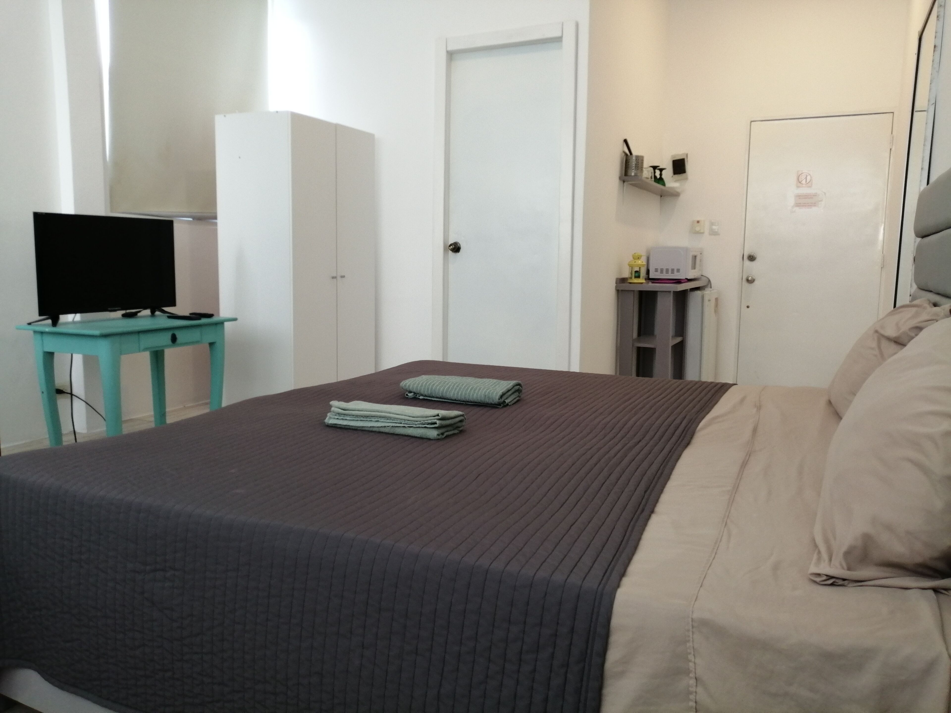 A bedroom with a bed, a desk with a television, a wardrobe, and a small shelf with items.