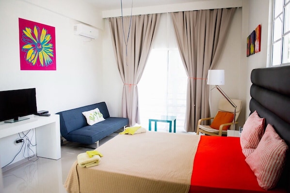 A modern hotel room with a bed, a desk with a TV, a sofa, and a chair.
