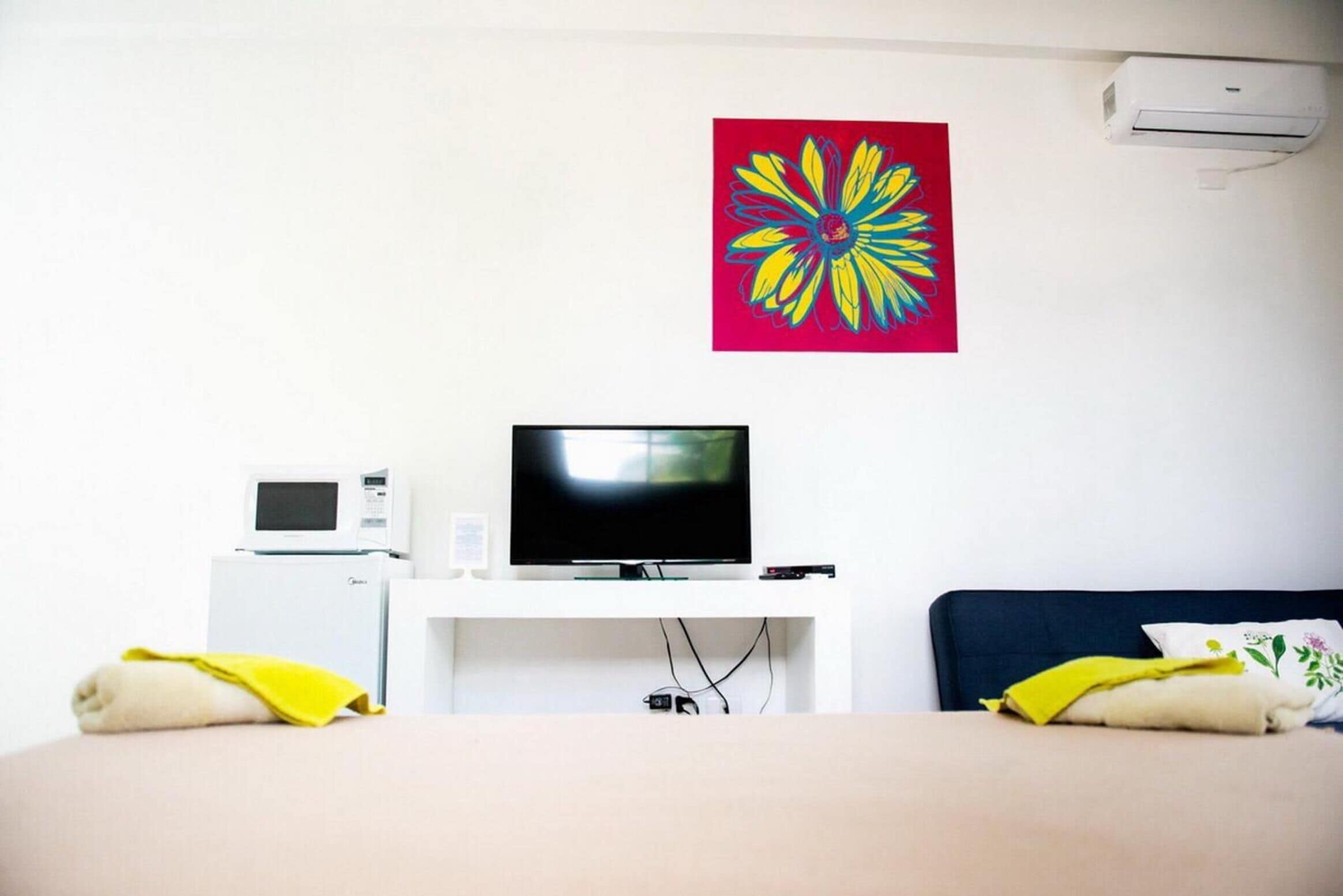 Ein Hotelzimmer mit einem Bett, einem Fernseher, einer Mikrowelle und einem farbenfrohen Blumenbild an der Wand.