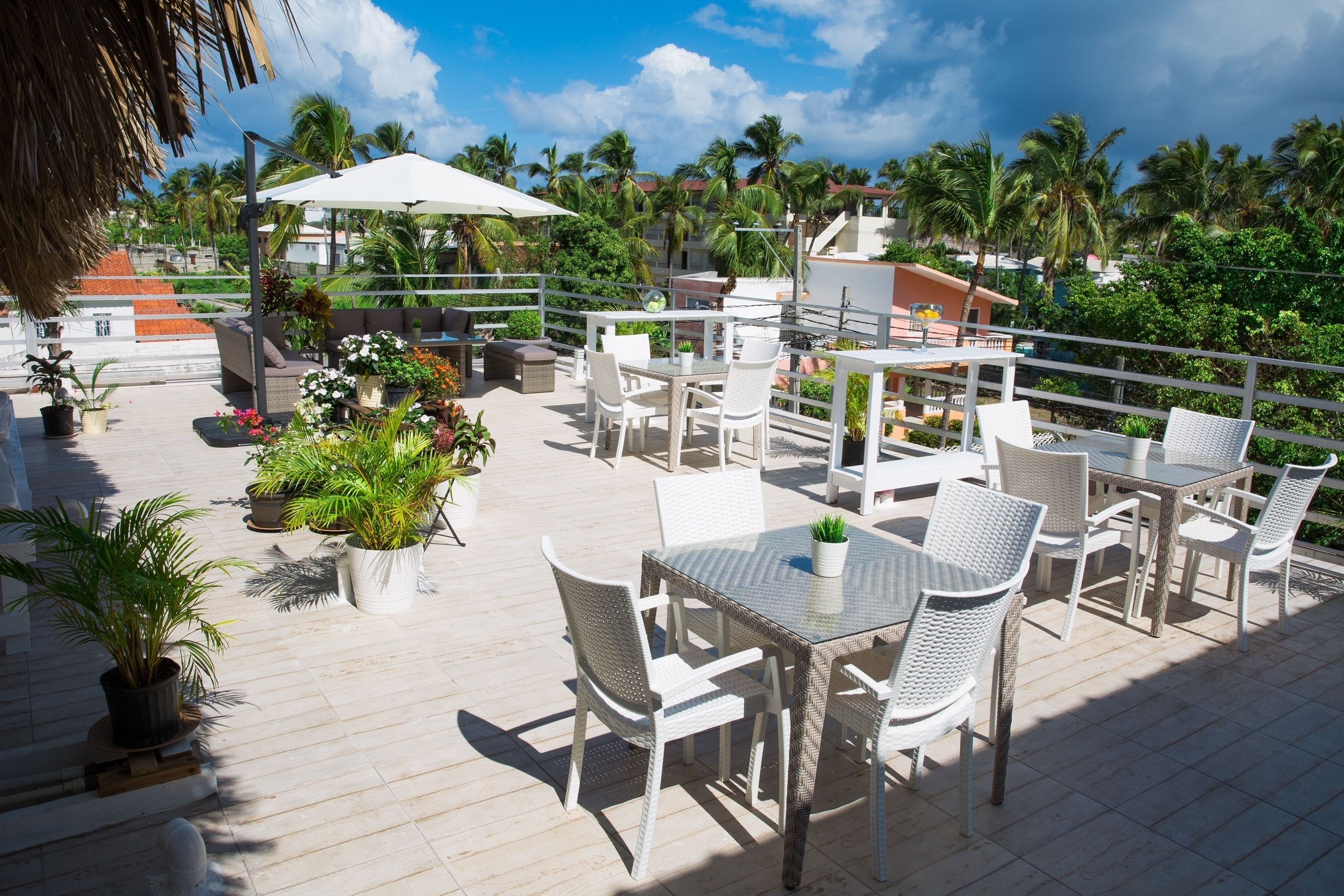 An outdoor patio area with white wicker furniture, potted plants, and a white umbrella.