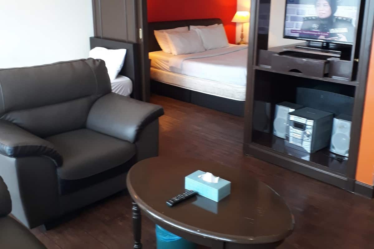 Ett modernt hotellrum med en soffa, ett runt soffbord med en fjärrkontroll och näsdukar, en säng med vita sängkläder, en tv på ett stativ och en röd accentvägg.
