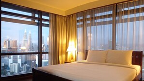 Habitación de hotel con una cama grande, una mesita de noche, una lámpara y vistas a la ciudad.