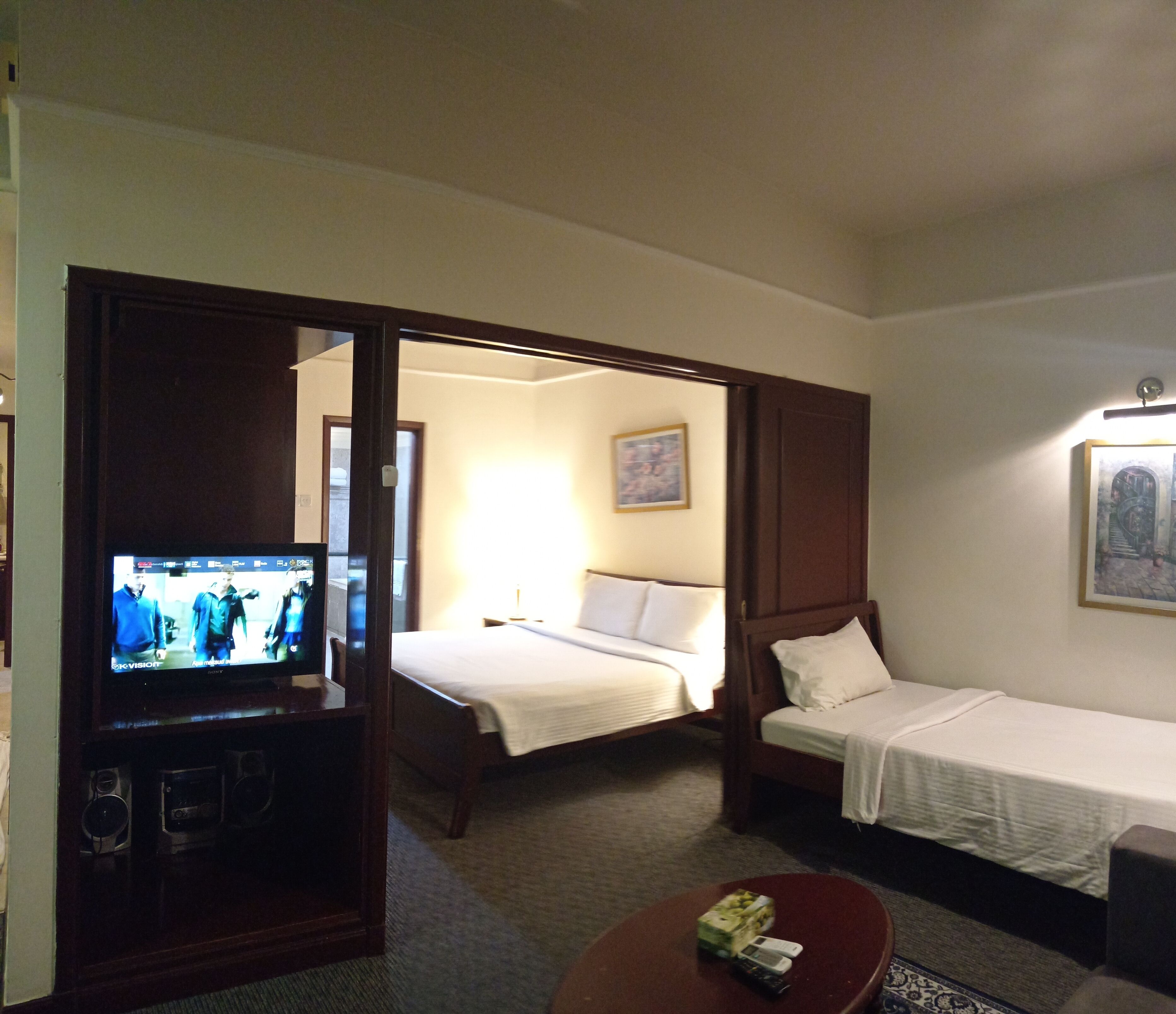 A hotel room with a TV, two beds, a small table, and a painting on the wall.