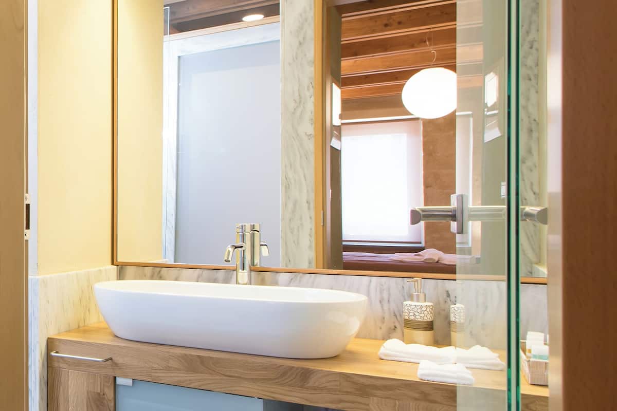 A modern bathroom with a large white sink, wooden vanity, and a glass shower enclosure.