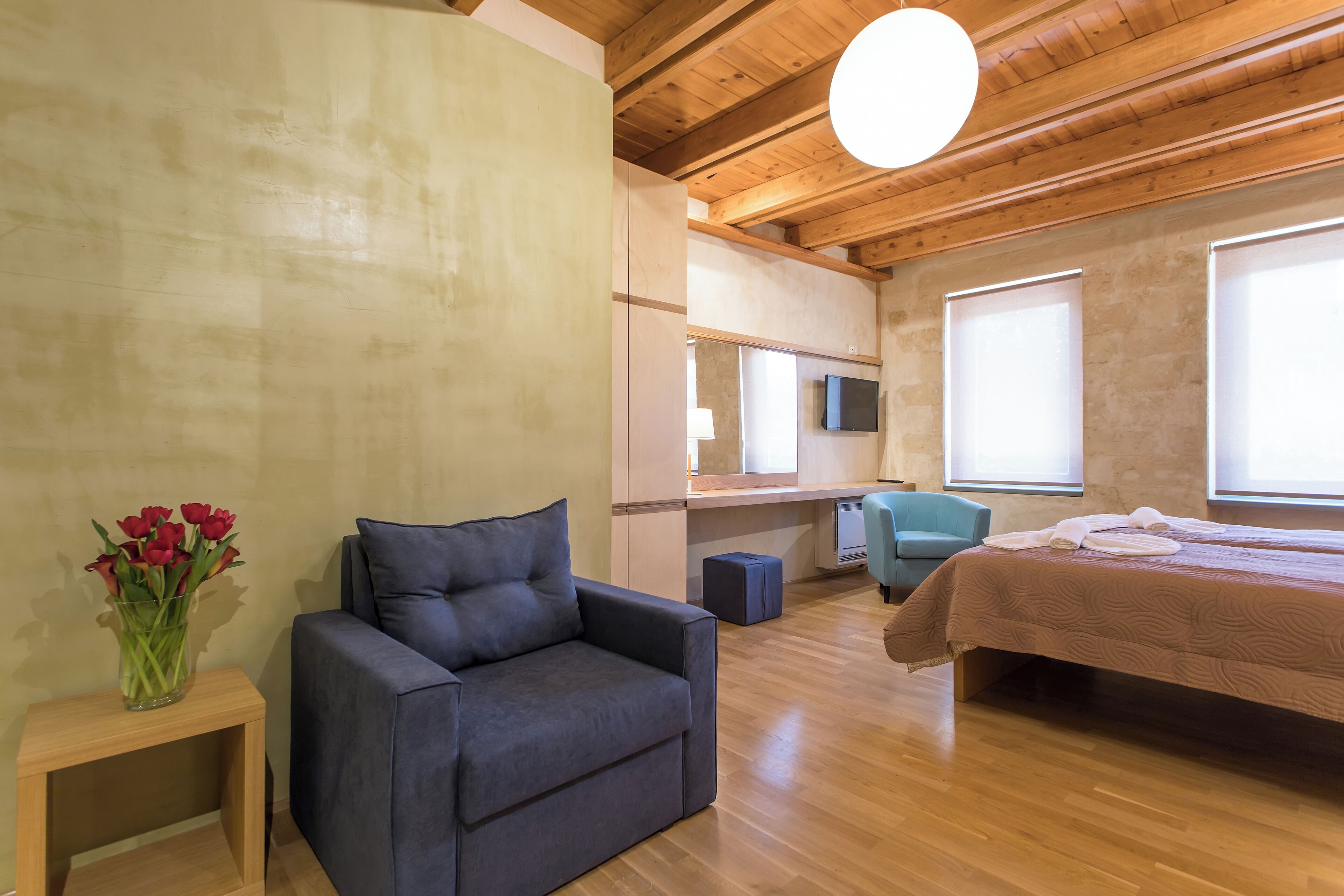 Una habitación moderna con techo de madera, una cama, un sofá, una mesita con un jarrón de flores y un televisor en la pared.