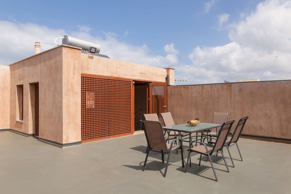 An outdoor patio with a table and chairs, a water tank on the roof, and a wooden fence. - Polixeny's Suites (Chania)