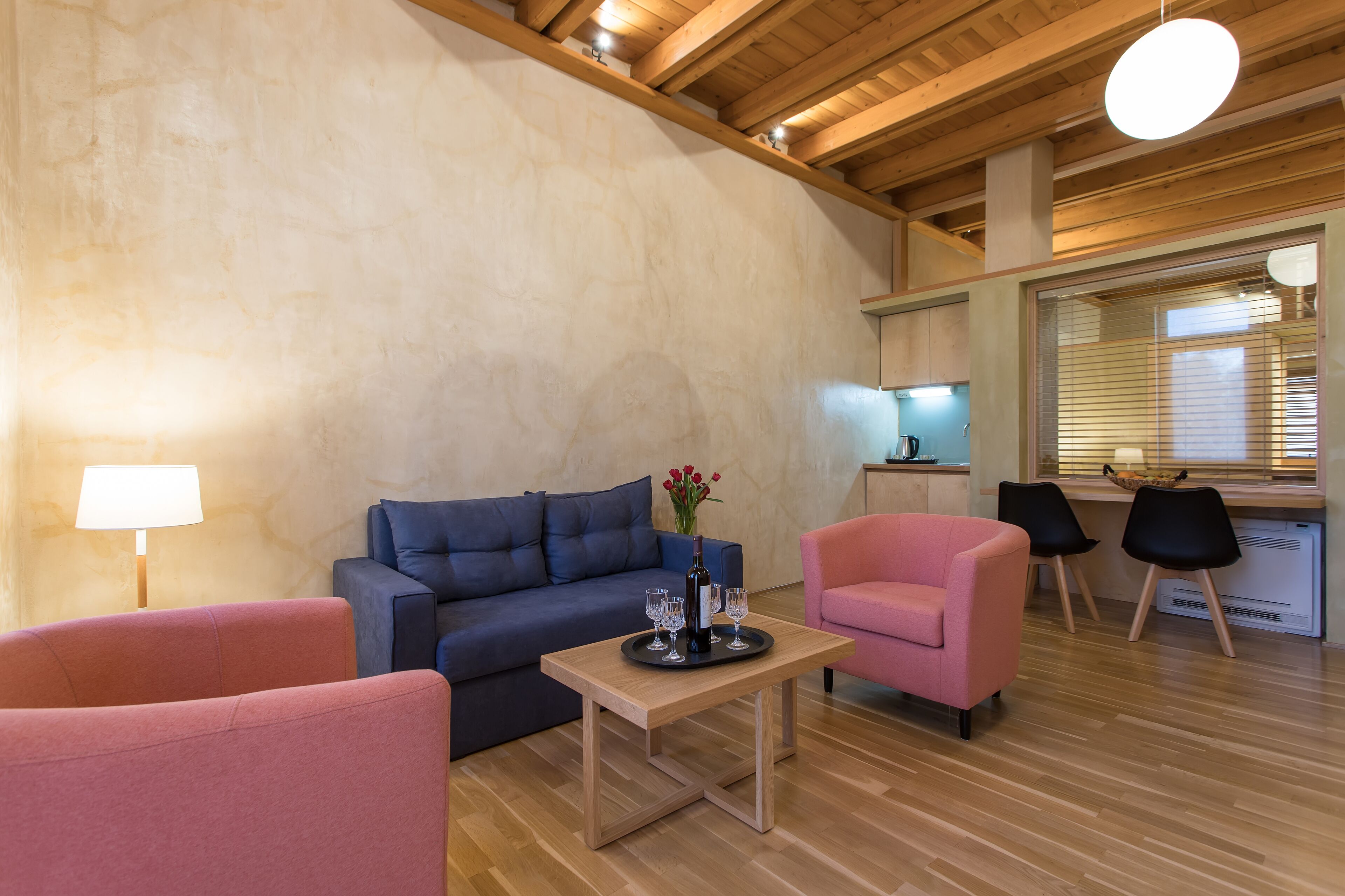 Een woonkamer met een houten tafel, een bank, een roze fauteuil en een blauwe bank.