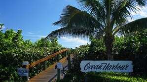 A pathway leading to a sign reading "Ocean Harbour" with a wooden bridge and lush greenery. - Hutchinson Island North Beach/Lagoon Access - First Floor Unit (Fort Pierce)