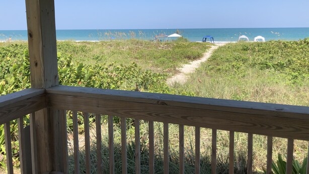 A wooden deck with a thatched roof overlooking a beach with a clear view of the ocean and beach umbrellas. - Hutchinson Island North Beach/Lagoon Access - First Floor Unit (Fort Pierce)