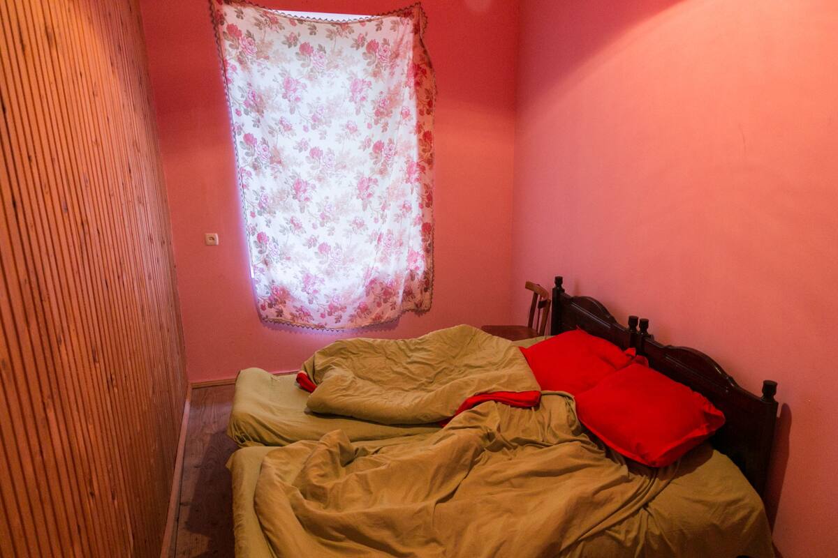 Een slaapkamer met een enkel bed, een houten hoofdeinde, een bloemen gordijn en een houten vloer.