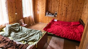 Een kamer met houten lambrisering en twee bedden, waarvan er één een groene deken heeft en de andere een rode.