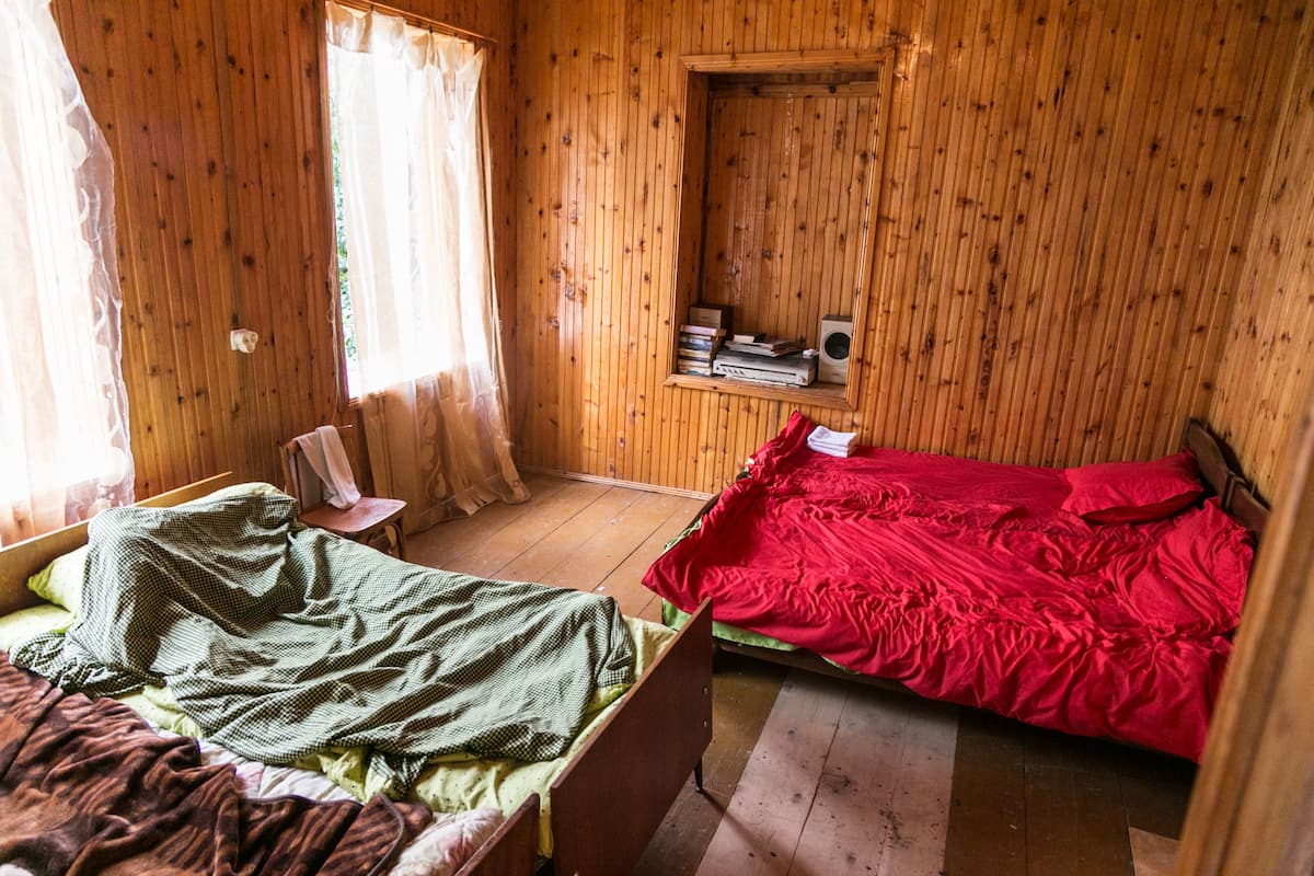 Een kamer met houten lambrisering en twee bedden, waarvan er één een groene deken heeft en de andere een rode.