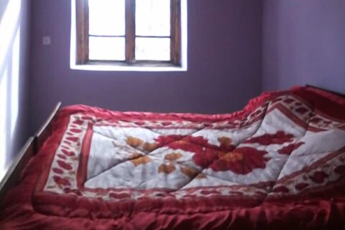 Een kamer met een enkel bed, een raam en een paarse muur.