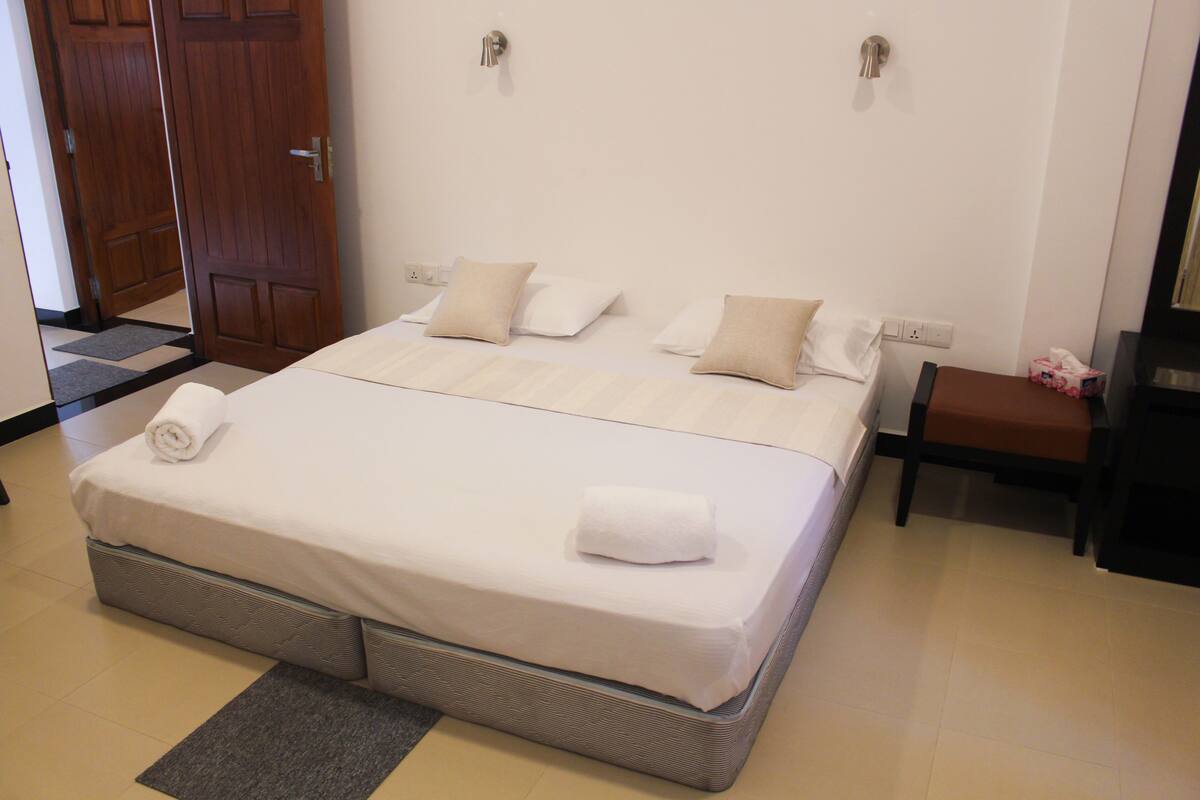 A neatly made bed with a grey mattress, white linens, and two rolled towels.