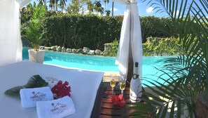 Un área junto a la piscina con una cama, toallas, una botella de champán y copas.