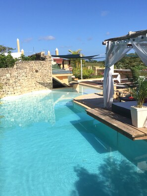 A clear blue pool with a stone wall on one side and a wooden deck with a pergola on the other. - Cabrera Chalet (Cabrera)