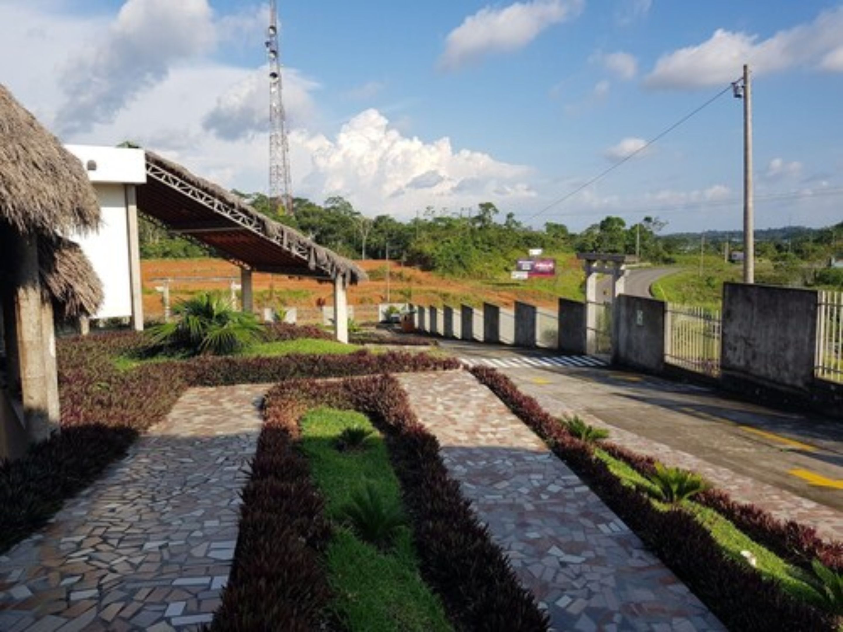 A paved pathway with a thatched-roof structure, a metal staircase, and a road with a guardrail.