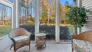 Eine überdachte Terrasse mit Korbmöbeln und Blick auf Bäume und einen Garten.