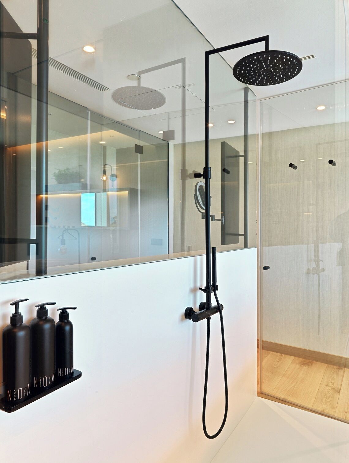 Un baño moderno con cabina de ducha de vidrio, un espejo grande y tres botellas negras en una estantería.