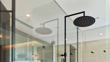 Un baño moderno con cabina de ducha de vidrio, un espejo grande y tres botellas negras en una estantería.