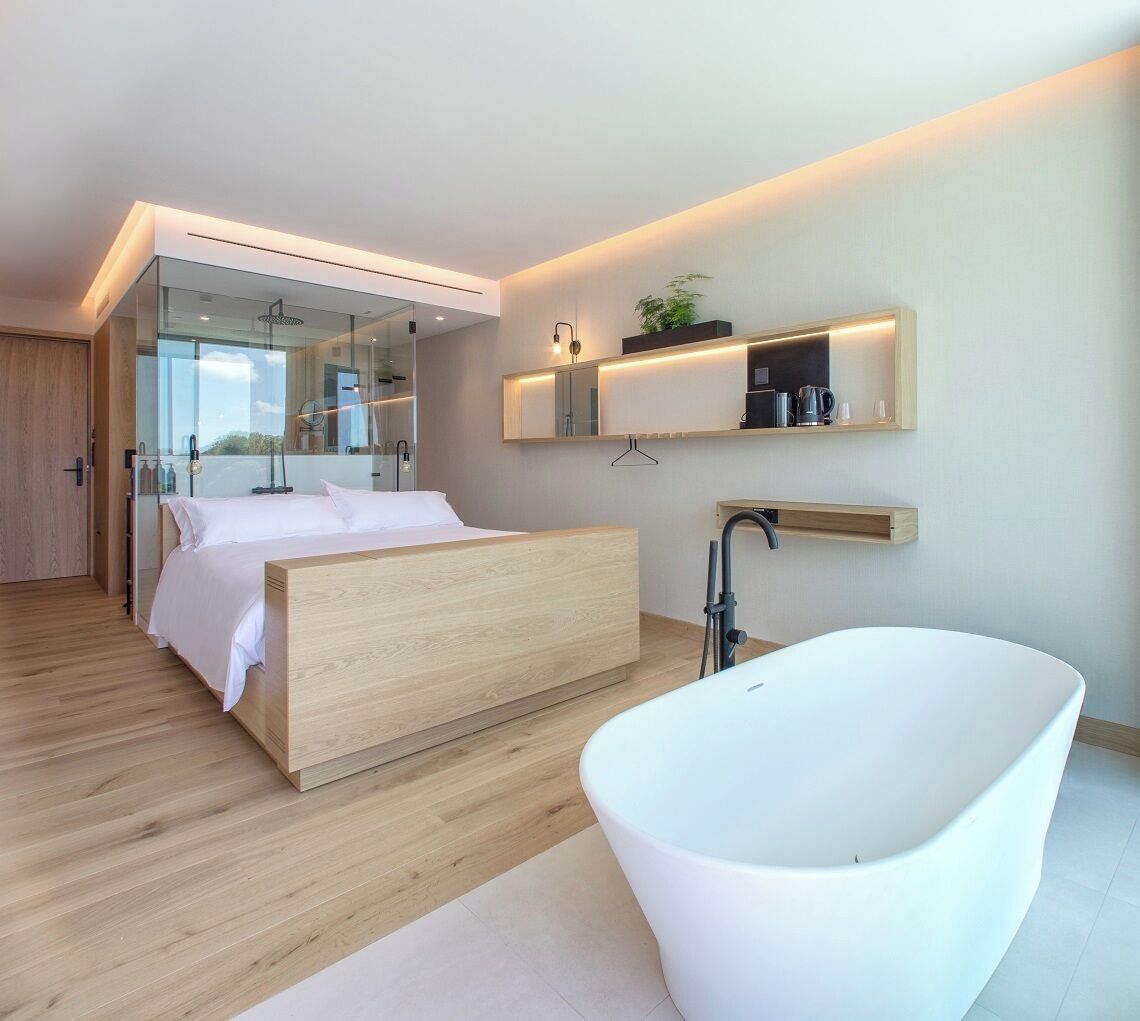 A modern bedroom with a large bed, a freestanding bathtub, and a glass-enclosed walk-in closet.
