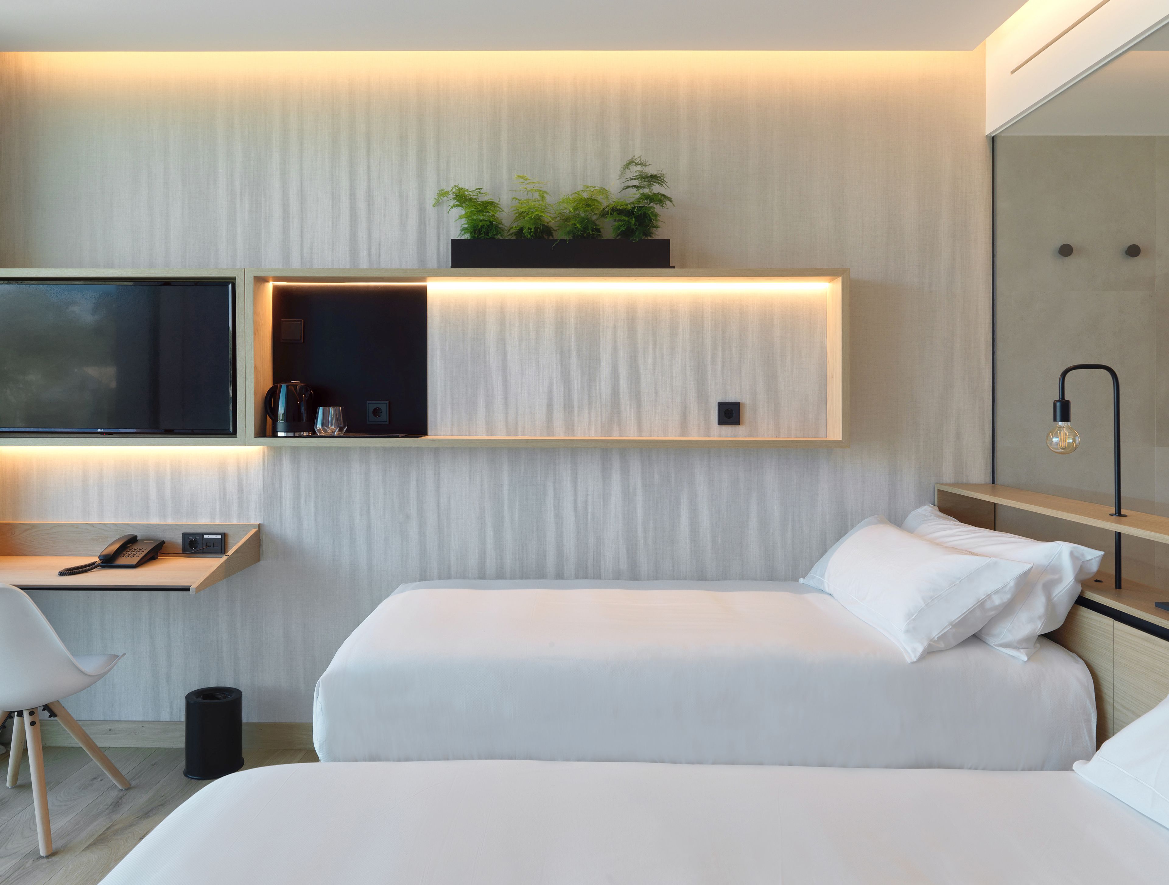 Una habitación de hotel moderna con una cama, una mesita de noche y un televisor montado.