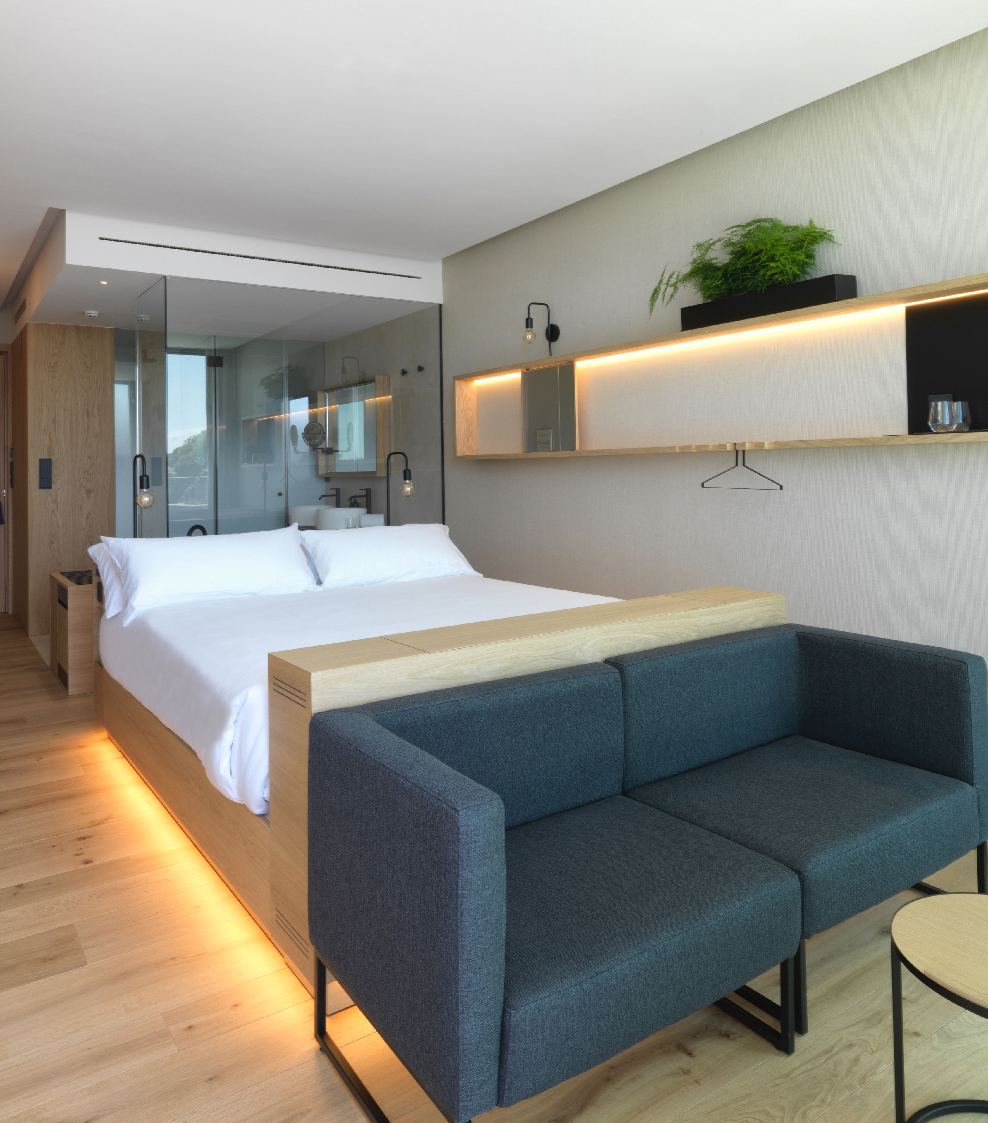 Una habitación de hotel moderna con una cama grande, un sofá, una mesita y un espejo.