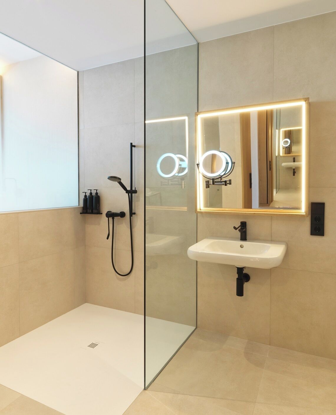 Un baño moderno con cabina de ducha de vidrio, lavamanos blanco y espejo con iluminación.