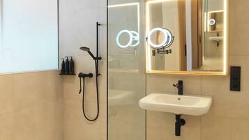 Un baño moderno con cabina de ducha de vidrio, lavamanos blanco y espejo con iluminación.