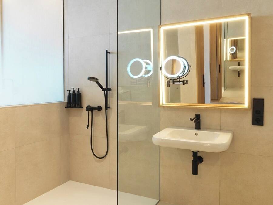Un baño moderno con cabina de ducha de vidrio, lavamanos blanco y espejo con iluminación.