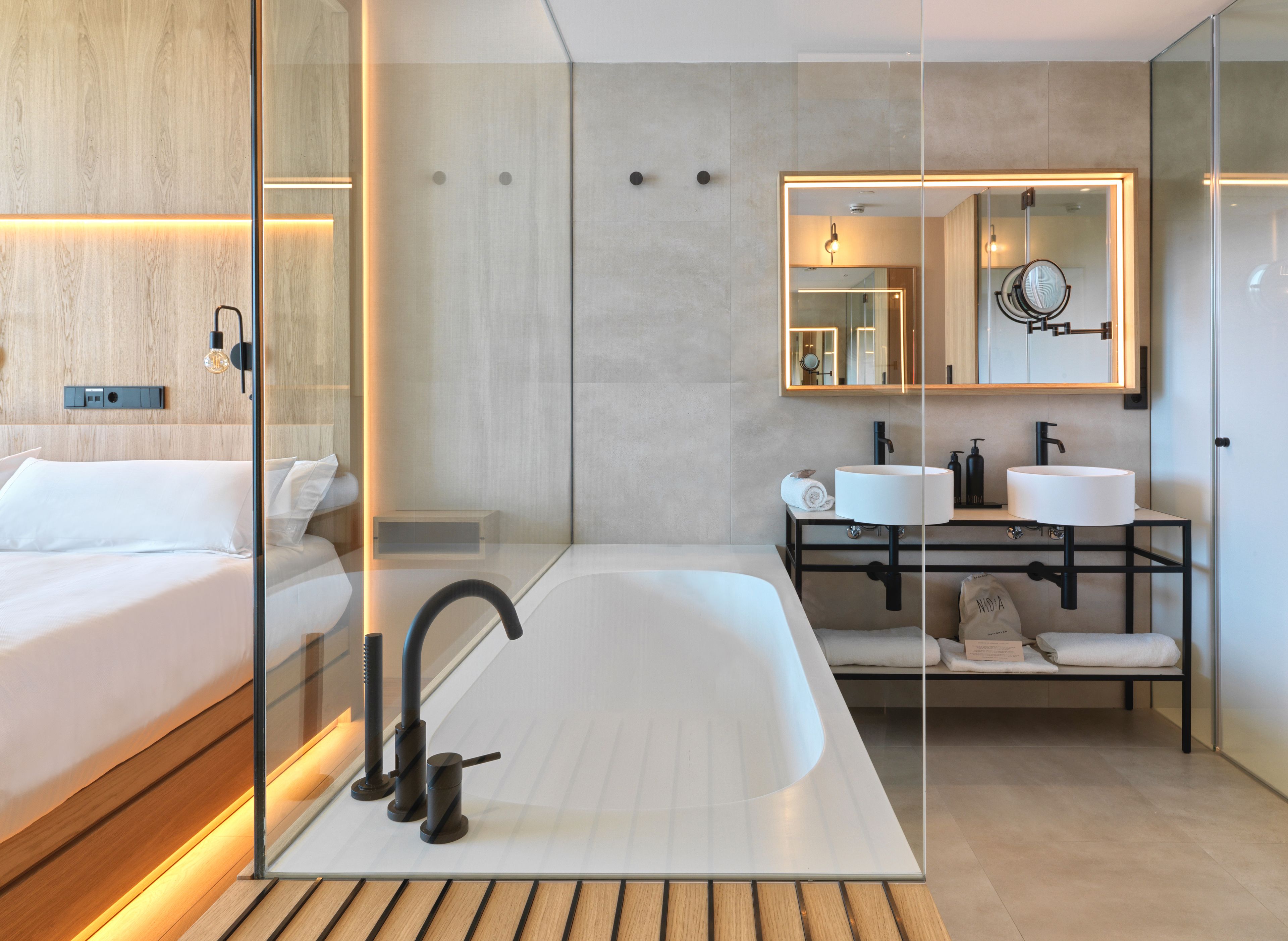 A modern hotel bathroom with a large bathtub, two sinks, and a mirror.