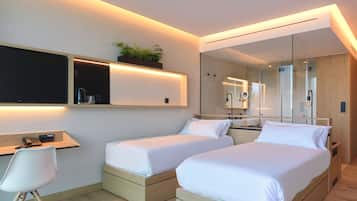 A modern hotel room with two beds, a desk, a chair, a large mirror, and a plant on the wall.