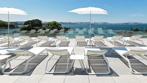 A rooftop pool area with sun loungers and umbrellas, overlooking a cityscape and body of water. - Noa Boutique Hotel (Oleiros)
