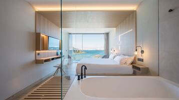 Habitación de hotel moderna con una cama grande, una bañera, un escritorio y vistas al mar.