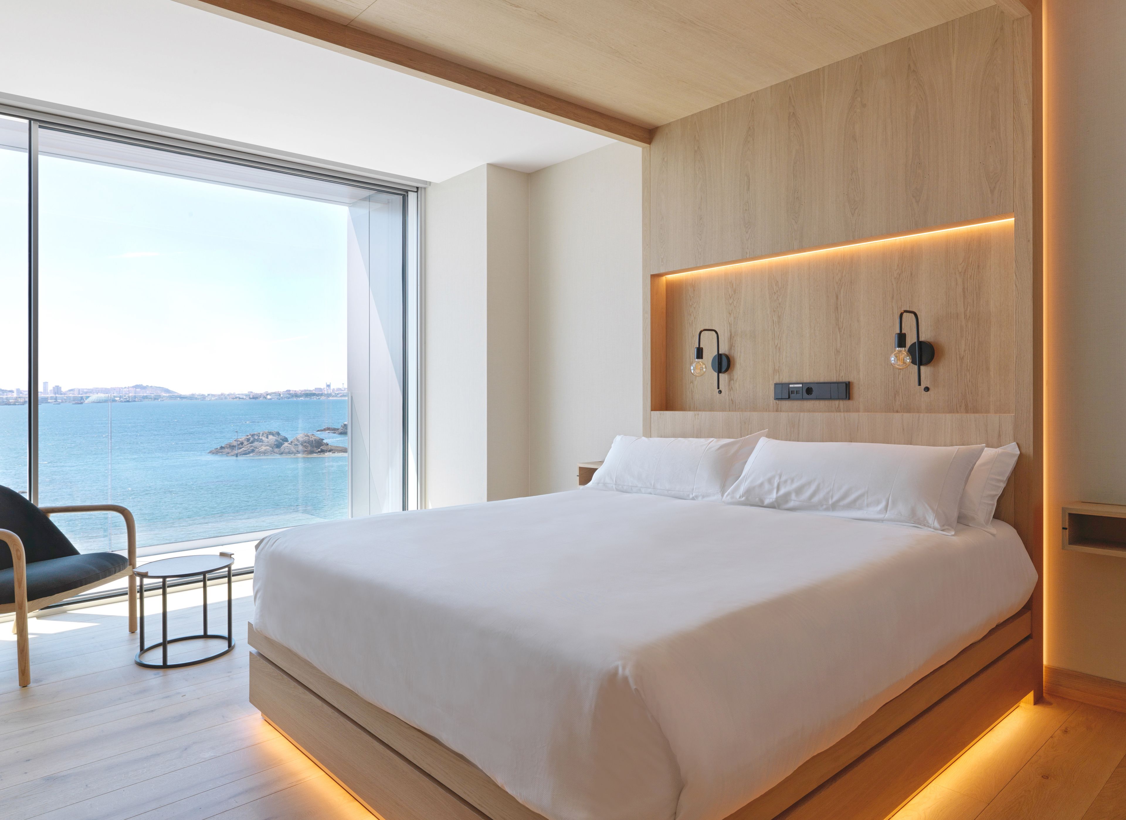 Un dormitorio moderno con una cama grande, una silla y vista al mar.