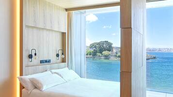 Un dormitori modern amb llit integrat, panells de fusta, vista al mar i un paisatge urbà de fons.