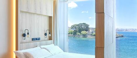 A modern bedroom with a built-in bed, wooden paneling, a view of the sea, and a cityscape in the background.