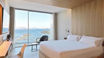 Una habitación de hotel moderna con una cama grande, un escritorio y una silla. La habitación tiene un ventanal con vistas al mar.