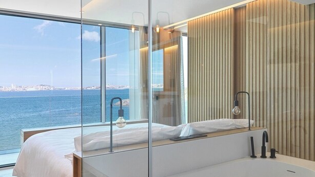 A modern bedroom with a large bed, a bathtub, and a view of the sea. - Noa Boutique Hotel (Oleiros)
