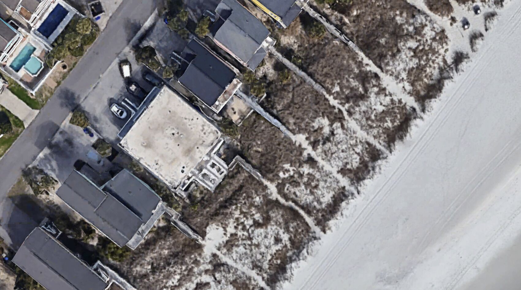 Ett flygbildsfoto av en fastighet vid kusten med flera byggnader, en swimmingpool och ett område med strand.