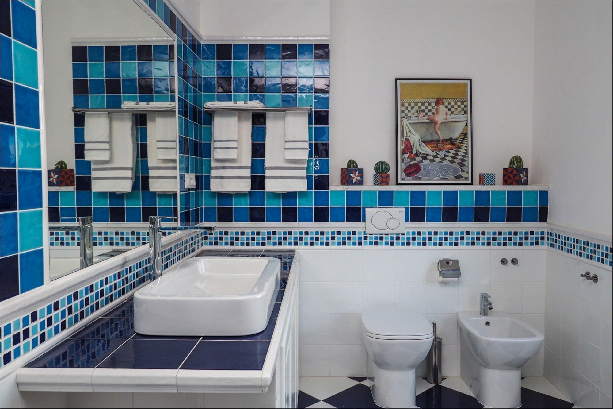 A bathroom with a large white bathtub, a toilet, and a bidet. The walls are tiled with blue and white tiles.