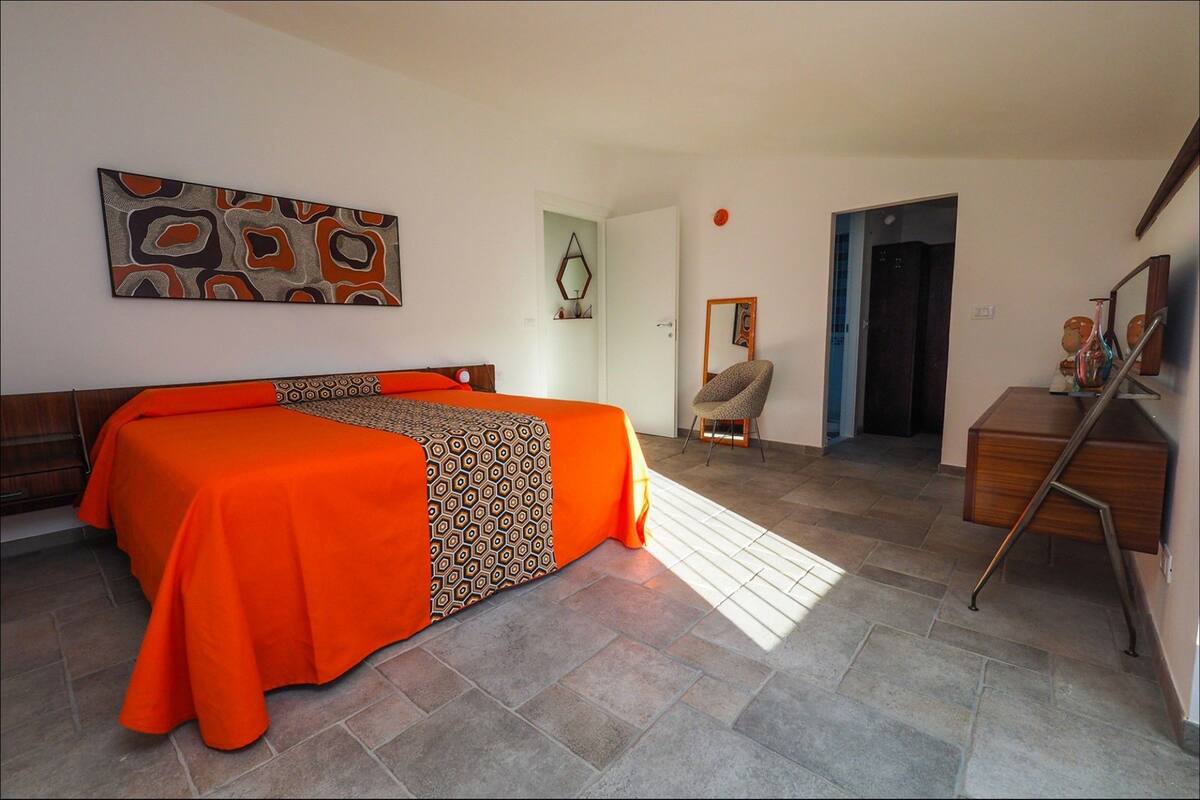 A hotel room with a bed, a desk, a chair, and a door leading to another room.