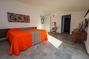 A hotel room with a bed, a desk, a chair, and a door leading to another room. - La Gazzeri Residence & Country House (Tagliolo Monferrato)